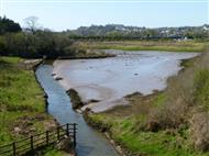 View over an area of rough ground with a stream and a large area of exposed mud